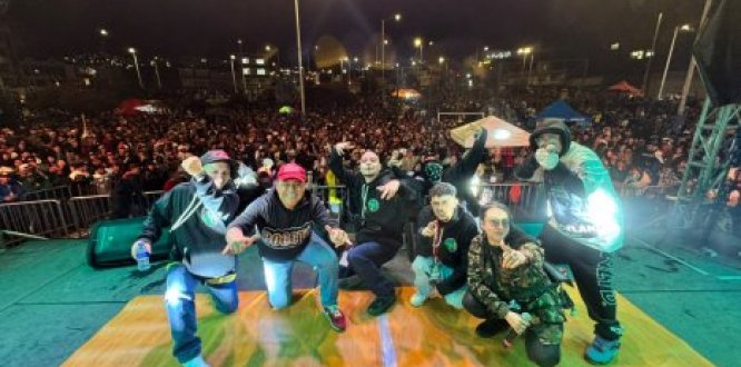 Artistas posan sobre el escenario frente a una multitud durante un festival de hip hop nocturno, en un ambiente lleno de energía, música y cultura urbana.