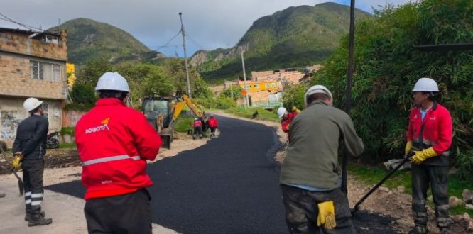 Se adelanta una intervención vial con instalación de mezcla asfáltica en un sector residencial de ladera, con presencia de maquinaria, personal técnico y acompañamiento institucional.