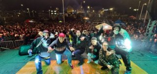 Artistas posan sobre el escenario frente a una multitud durante un festival de hip hop nocturno, en un ambiente lleno de energía, música y cultura urbana.