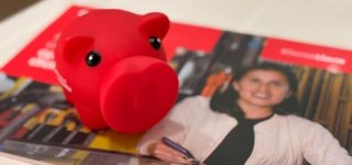 Alcancía roja sobre revista institucional, símbolo de ahorro y fortalecimiento del emprendimiento.